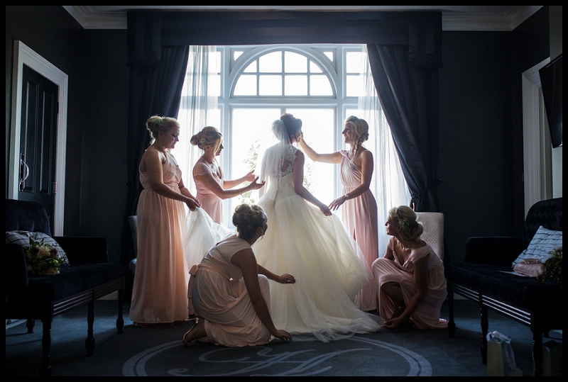 Bridesmaids adjusting brides dress at Paddocks House in front of window