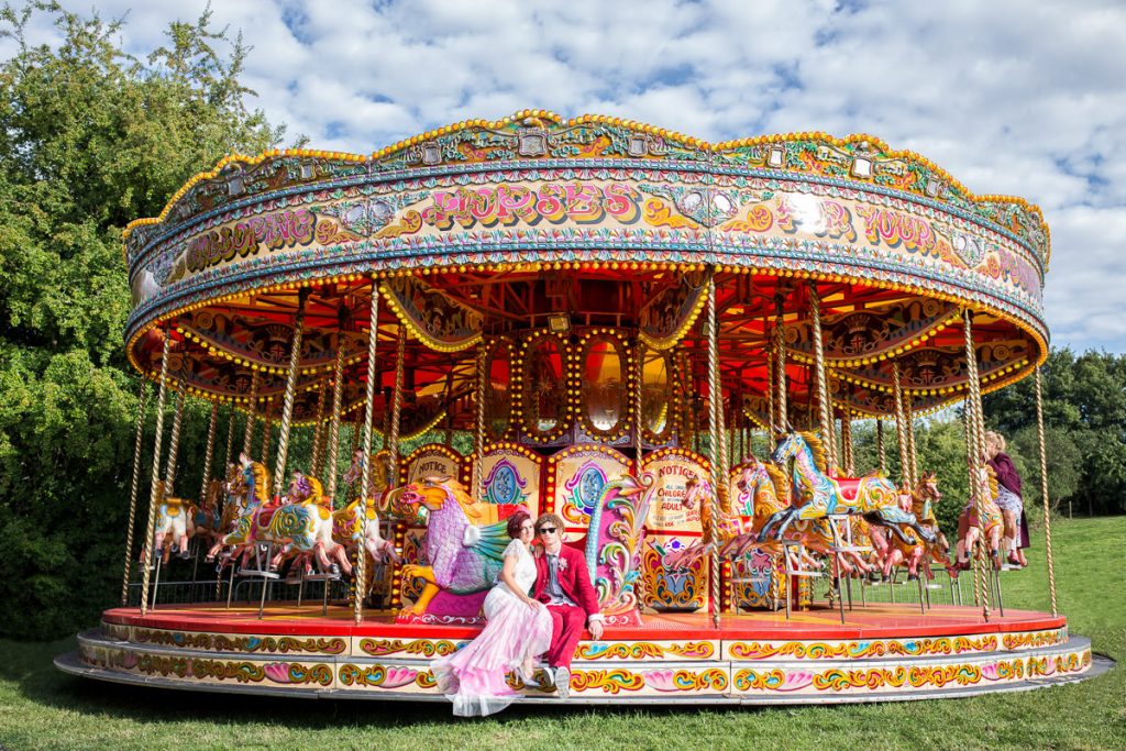 Alternative Bride and groom sitting on fairground carousel